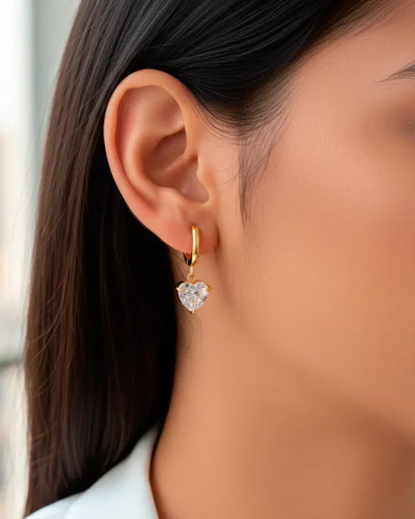 Gold heart drop earrings with crystal detail, worn on ear, minimalist heart jewelry by Cutu Store.