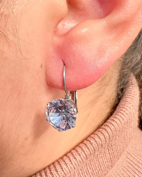 Silver drop earrings with clear round stone worn on ear, angled close-up view in Malta